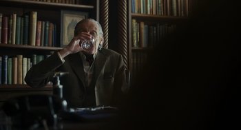 Movie still from “Flux Gourmet” (2022), directed by Peter Strickland – An older man drinking a glass of water; Medium shot, Over the shoulder angle