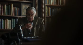 Movie still from “Flux Gourmet” (2022), directed by Peter Strickland – An older man sitting at a table with a glass of wine; Medium shot, Over the shoulder angle
