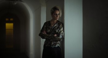 Movie still from “Flux Gourmet” (2022), directed by Peter Strickland – A woman standing in front of a wall with her arms crossed; Medium shot, Low angle