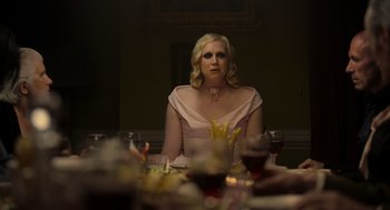 Movie still from “Flux Gourmet” (2022), directed by Peter Strickland – A woman sitting at a dinner table with a glass of wine; Medium shot, Over the shoulder angle