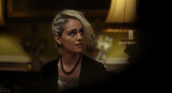 Movie still from “Flux Gourmet” (2022), directed by Peter Strickland – A woman in a black jacket and a black necklace; Close Up shot, Over the shoulder angle