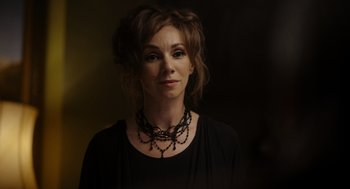 Movie still from “Flux Gourmet” (2022), directed by Peter Strickland – A woman wearing a black shirt and a black necklace; Close Up shot, High angle