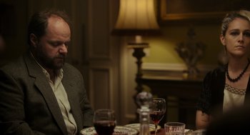 Movie still from “Flux Gourmet” (2022), directed by Peter Strickland – A man sitting at a table with a glass of red wine; Medium shot, Over the shoulder angle