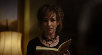 Movie still from “Flux Gourmet” (2022), directed by Peter Strickland – A woman wearing a necklace holding an open book; Close Up shot, High angle