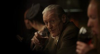 Movie still from “Flux Gourmet” (2022), directed by Peter Strickland – An older man holding a glass of wine in his hand; Close Up shot, Low angle