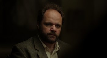 Movie still from “Flux Gourmet” (2022), directed by Peter Strickland – A person wearing a suit and tie; Close Up shot, Low angle