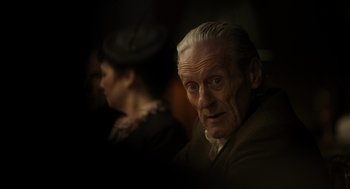 Movie still from “Flux Gourmet” (2022), directed by Peter Strickland – An old man and a young woman are looking at the camera; Close Up shot, Low angle