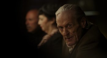 Movie still from “Flux Gourmet” (2022), directed by Peter Strickland – A man and a woman standing next to each other in front of another man; Close Up shot, Low angle