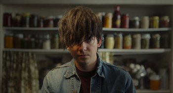 Movie still from “Flux Gourmet” (2022), directed by Peter Strickland – A young man with long hair is posing for a picture; Close Up shot, Over the shoulder angle