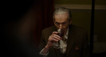 Movie still from “Flux Gourmet” (2022), directed by Peter Strickland – An older man drinking a glass of wine; Close Up shot, Over the shoulder angle