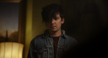 Movie still from “Flux Gourmet” (2022), directed by Peter Strickland – A young man with long black hair wearing a jean jacket; Close Up shot, High angle