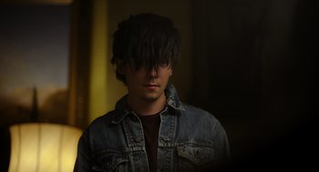 Movie still from “Flux Gourmet” (2022), directed by Peter Strickland – A young man in a denim jacket looking at the camera; Close Up shot, Over the shoulder angle