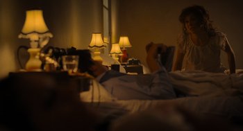 Movie still from “Flux Gourmet” (2022), directed by Peter Strickland – A man laying in bed next to two lamps; Medium shot, Over the shoulder angle