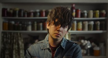 Movie still from “Flux Gourmet” (2022), directed by Peter Strickland – A young man with long hair and a denim jacket; Close Up shot, Low angle
