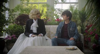 Movie still from “Flux Gourmet” (2022), directed by Peter Strickland – A man and a woman sitting on a white couch; Medium shot, Over the shoulder angle