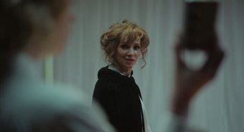 Movie still from “Flux Gourmet” (2022), directed by Peter Strickland – A woman in a black jacket is looking at the camera; Close Up shot, Over the shoulder angle