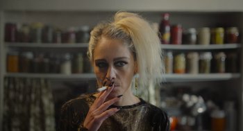Movie still from “Flux Gourmet” (2022), directed by Peter Strickland – A woman smoking a cigarette in a room; Close Up shot, Low angle