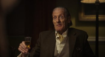 Movie still from “Flux Gourmet” (2022), directed by Peter Strickland – An older man with a glass of wine; Close Up shot, Low angle