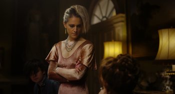 Movie still from “Flux Gourmet” (2022), directed by Peter Strickland – A woman in a pink dress is standing in front of other people; Medium shot, Over the shoulder angle