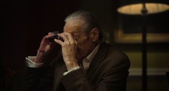 Movie still from “Flux Gourmet” (2022), directed by Peter Strickland – An older man taking a picture with a cell phone; Close Up shot, Low angle