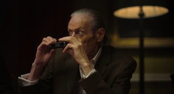 Movie still from “Flux Gourmet” (2022), directed by Peter Strickland – An older man is holding a cell phone up to his face; Close Up shot, Low angle