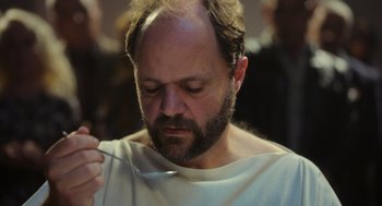 Movie still from “Flux Gourmet” (2022), directed by Peter Strickland – A man with a beard is holding a fork; Close Up shot, Low angle