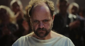 Movie still from “Flux Gourmet” (2022), directed by Peter Strickland – A man with a beard is looking at the camera; Close Up shot, Low angle