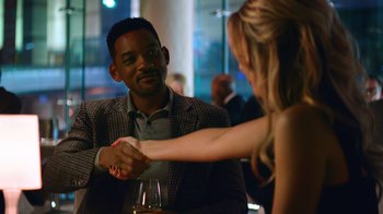 Movie still from “Focus” (2015), directed by John Requa – A man and a woman shaking hands over a glass of wine; Medium shot, Over the shoulder angle