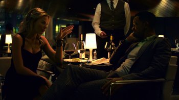 Movie still from “Focus” (2015), directed by John Requa – A group of people sitting around a table with wine glasses; Medium shot, Over the shoulder angle