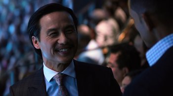 Movie still from “Focus” (2015), directed by John Requa – A man in a suit and tie smiling for the camera; Close Up shot, Over the shoulder angle