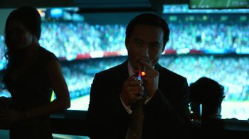 Movie still from “Focus” (2015), directed by John Requa – A man in a suit and tie lighting a cigarette; Medium shot, High angle