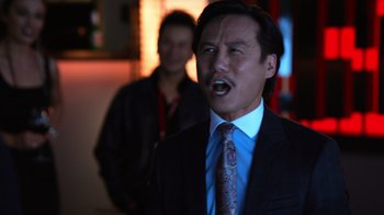 Movie still from “Focus” (2015), directed by John Requa – A man in a suit and tie with a man in the background; Close Up shot, Over the shoulder angle