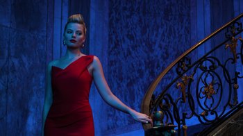 Movie still from “Focus” (2015), directed by John Requa – A woman in a red dress standing in front of an iron gate; Medium shot, Low angle