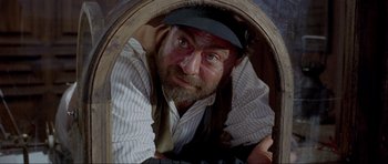 Movie still from “For a Few Dollars More” (1965), directed by Sergio Leone – A man with a beard wearing a hat looking through a hole in the wall; Close Up shot, Low angle