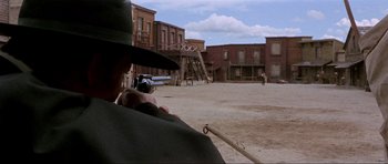 Movie still from “For a Few Dollars More” (1965), directed by Sergio Leone – A man holding a gun while standing on a dirt field; Wide shot, Over the shoulder angle