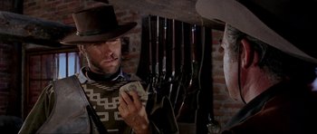 Movie still from “For a Few Dollars More” (1965), directed by Sergio Leone – A man in a cowboy hat holding a dollar bill in his hand; Close Up shot, Over the shoulder angle
