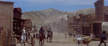 Movie still from “For a Few Dollars More” (1965), directed by Sergio Leone – A group of men riding horses down a dirt road; Extreme Wide shot, Low angle