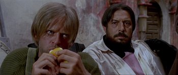 Movie still from “For a Few Dollars More” (1965), directed by Sergio Leone – A man eating a piece of food next to another man; Close Up shot, Low angle