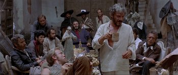 Movie still from “For a Few Dollars More” (1965), directed by Sergio Leone – A group of people sitting around a table eating food; Medium shot, Low angle
