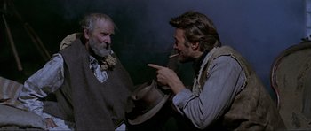 Movie still from “For a Few Dollars More” (1965), directed by Sergio Leone – A man smoking a cigarette while another man holds a hat; Medium shot, Over the shoulder angle