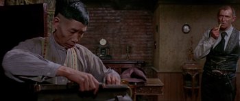 Movie still from “For a Few Dollars More” (1965), directed by Sergio Leone – An older asian man using a pair of scissors; Medium shot, Low angle