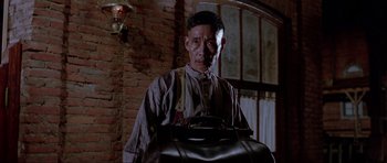 Movie still from “For a Few Dollars More” (1965), directed by Sergio Leone – An older man holding a black bag in a room; Medium shot, Low angle