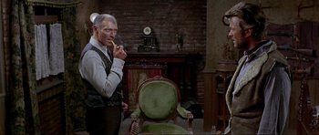 Movie still from “For a Few Dollars More” (1965), directed by Sergio Leone – An older man smoking a cigarette in a living room; Medium shot, Over the shoulder angle