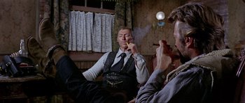 Movie still from “For a Few Dollars More” (1965), directed by Sergio Leone – Two men sitting in a room smoking a cigarette; Medium shot, Low angle
