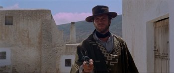 Movie still from “For a Few Dollars More” (1965), directed by Sergio Leone – A man holding a gun while wearing a hat; Medium shot, Low angle