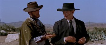Movie still from “For a Few Dollars More” (1965), directed by Sergio Leone – Two men in suits and hats are standing together; Medium shot, Low angle