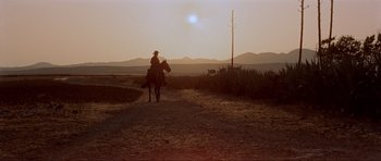 Movie still from “For a Few Dollars More” (1965), directed by Sergio Leone – A man riding a horse down a dirt road at sunset; Extreme Wide shot, Low angle