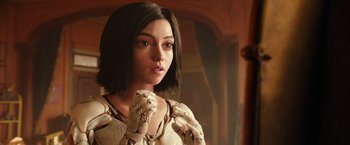 Movie still from “Alita: Battle Angel” (2019), directed by Robert Rodriguez – A young woman with short black hair is holding her hand up to her face; Close Up shot, Over the shoulder angle