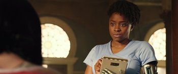 Movie still from “Alita: Battle Angel” (2019), directed by Robert Rodriguez – A woman holding a clipboard in front of a window; Close Up shot, Low angle