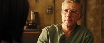 Movie still from “Alita: Battle Angel” (2019), directed by Robert Rodriguez – An older man wearing glasses sitting in a room; Close Up shot, Low angle